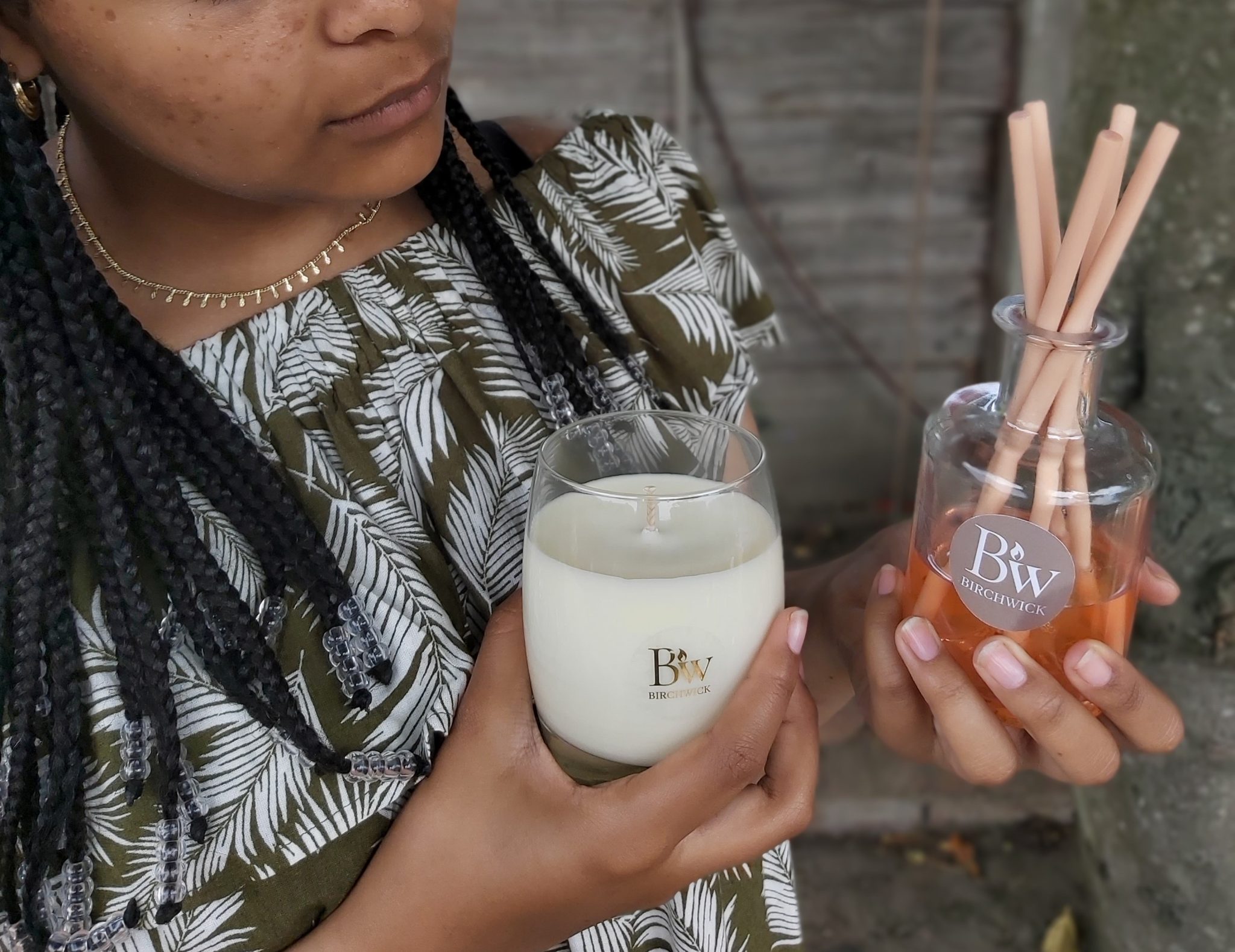 Hands holding a candle and diffuser against an earthy background.